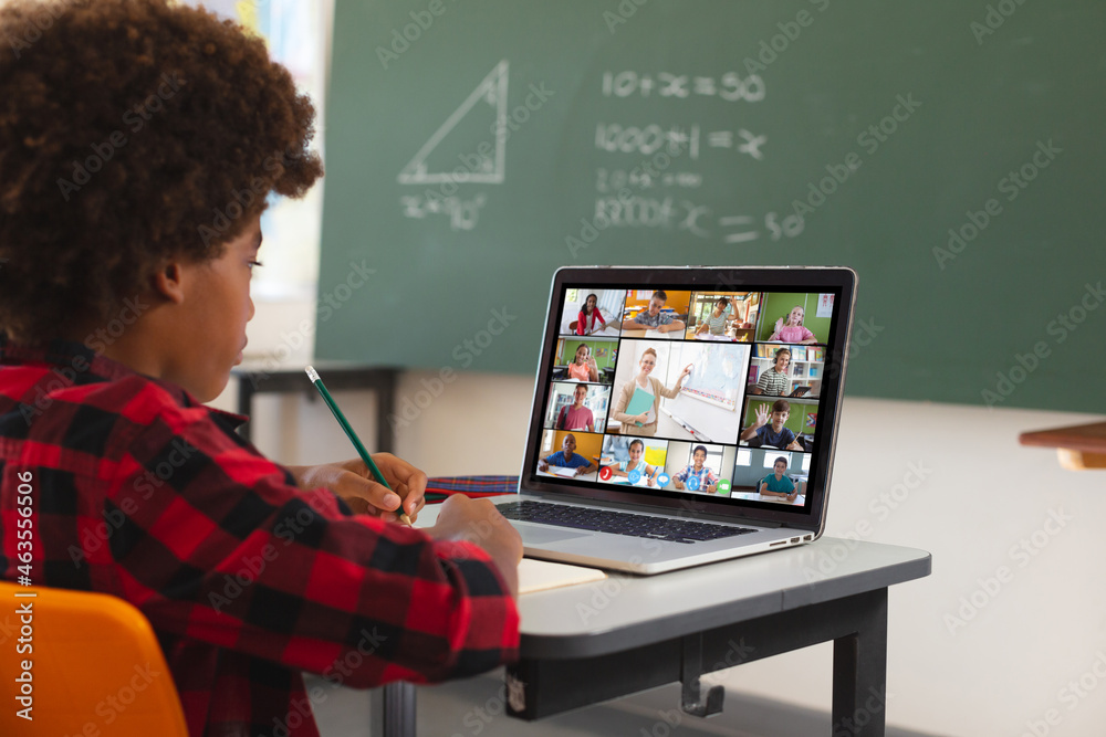 African american boy using laptop for video call, with diverse elementary school pupils on screen