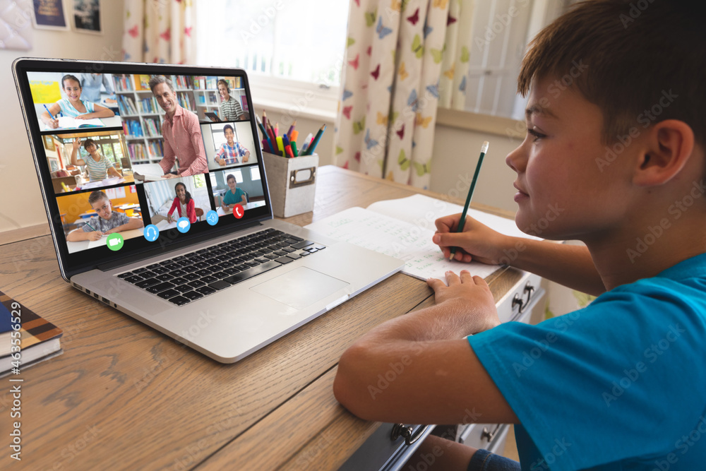 Caucasian boy using laptop for video call, with smiling diverse elementary school pupils on screen