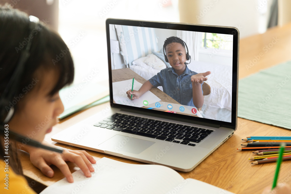 Asian girl using laptop for video call, with smiling elementary school pupil on screen