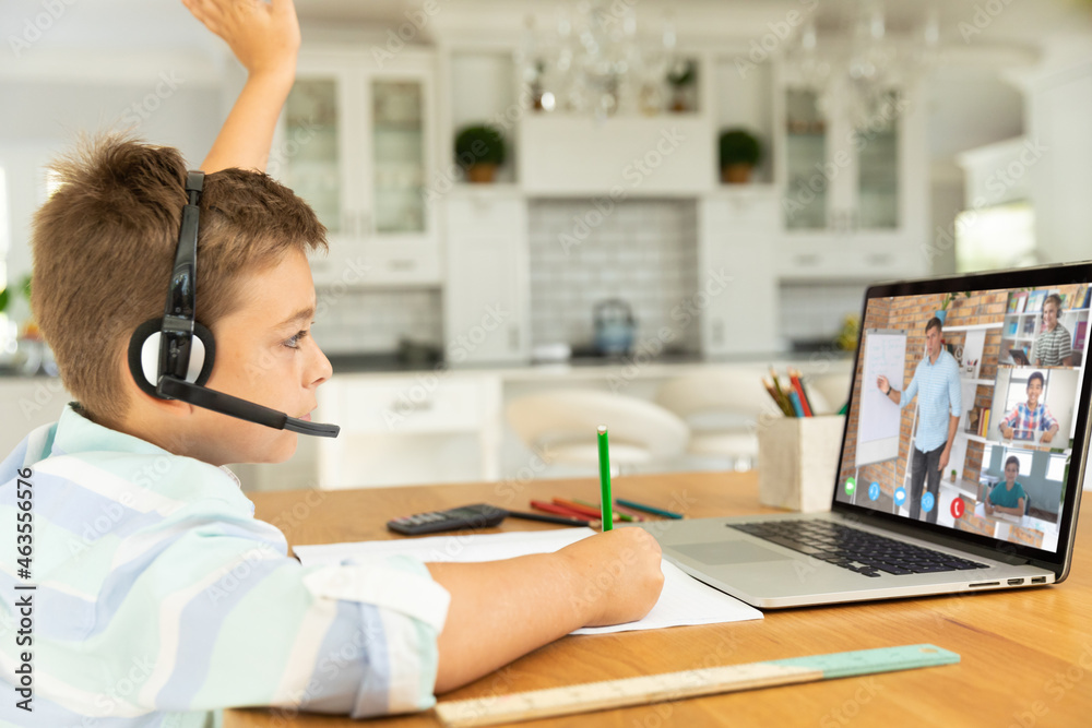 Caucasian boy raising hand for video call, with smiling diverse high school pupils on screen