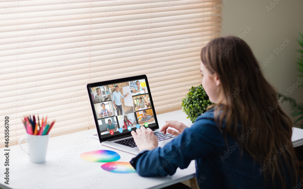 Caucasian girl using laptop for video call, with smiling diverse elementary school pupils on screen