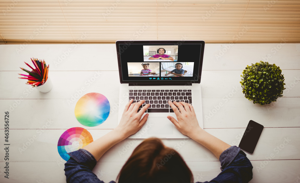 Caucasian woman using laptop for video call, with smiling diverse elementary school pupils on screen