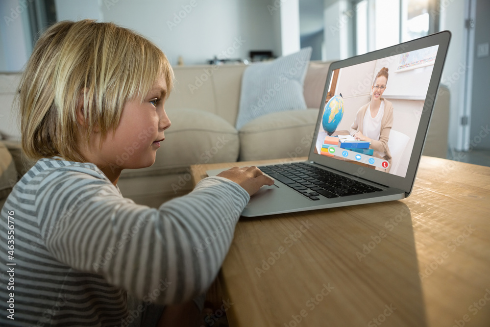 Caucasian boy using laptop for video call, with smiling female teacher on screen