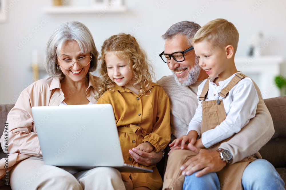 Smiling senior grandparents and cute little   grandchildren watching cartoons on laptop