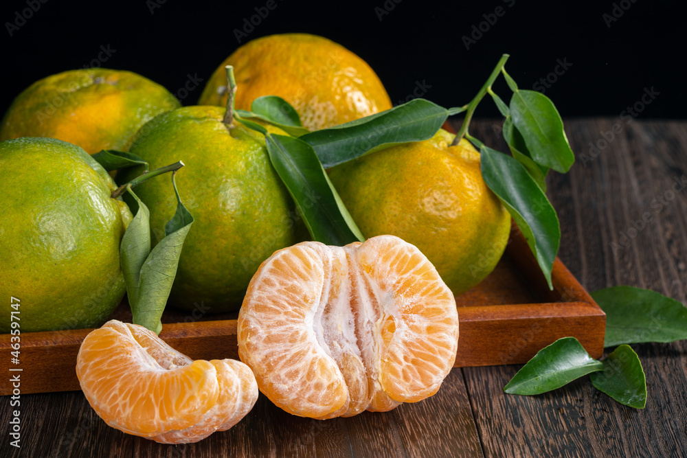 Fresh green tangerine on dark wooden table with black background.