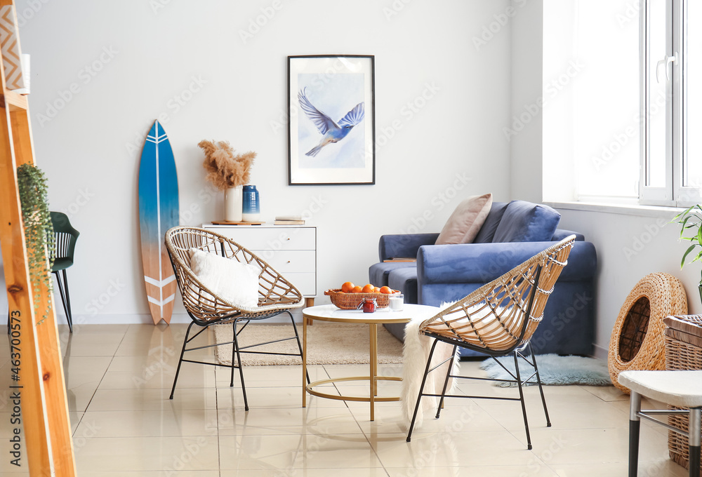 Interior of modern stylish room with table, wicker armchairs, sofa and surfboard