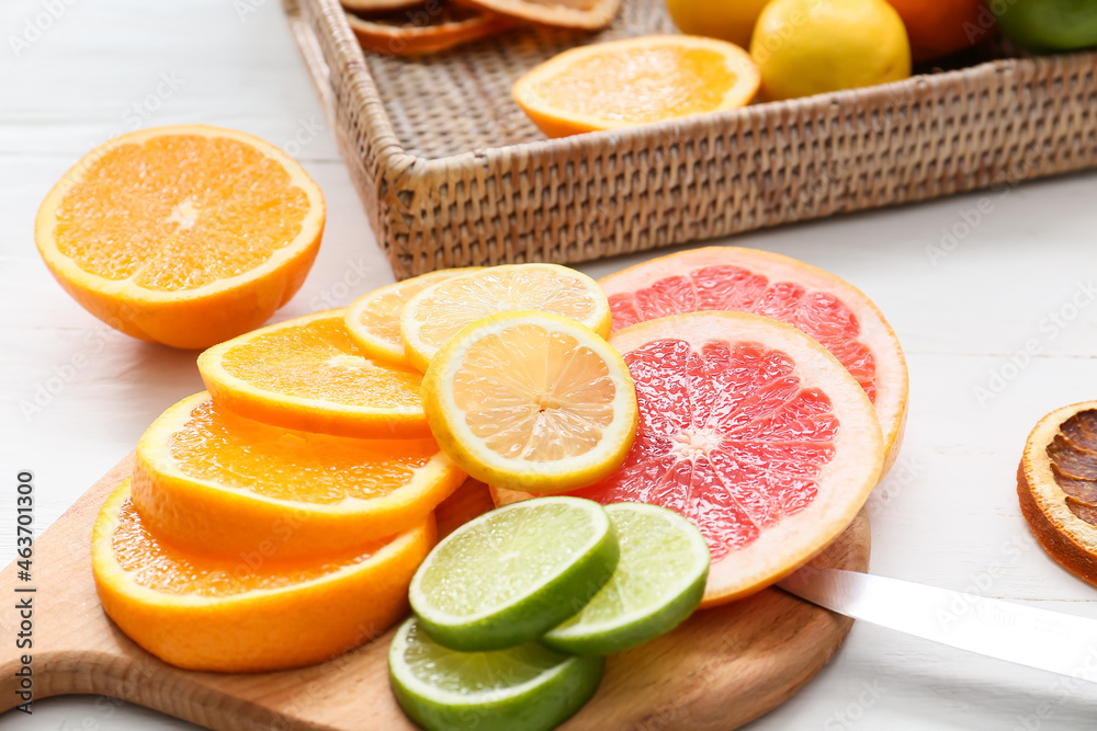 Board with slices of different citrus fruits on light wooden background, closeup