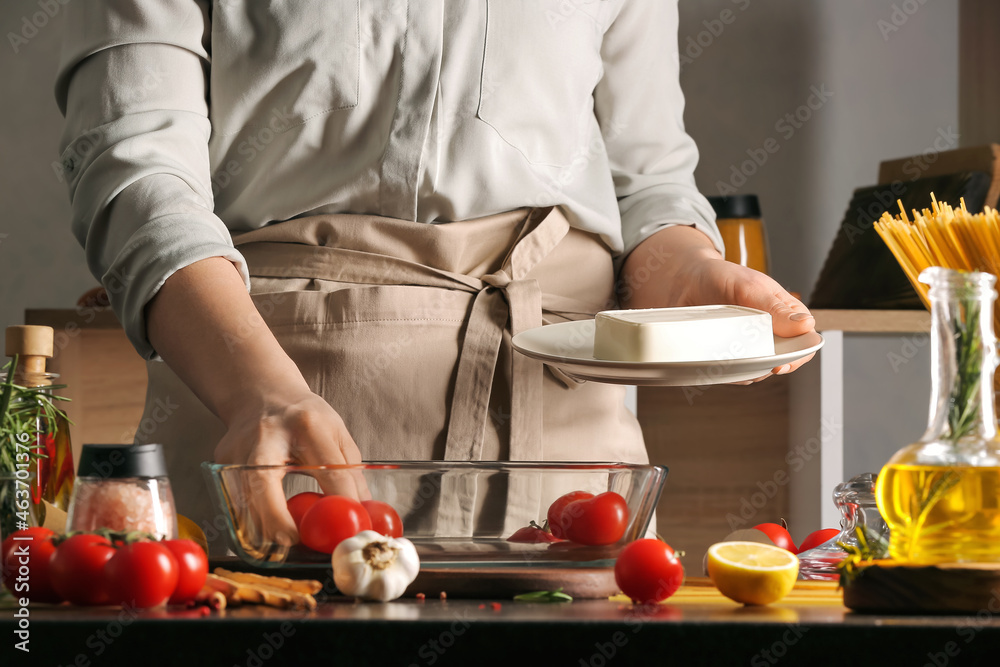 Woman with feta cheese and tomatoes in baking dish on table in kitchen