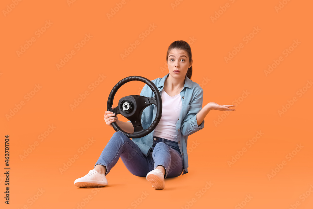 Confused young woman with steering wheel on color background