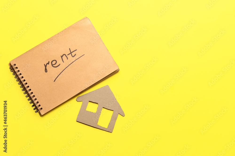 Notebook with word RENT and cardboard house on yellow background