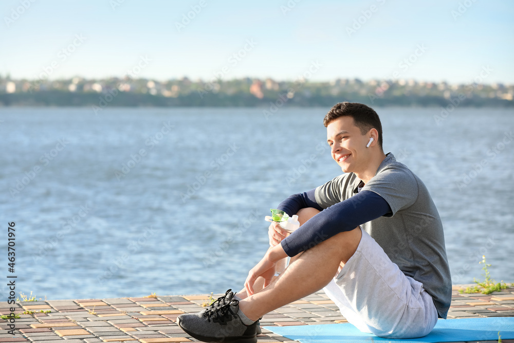 Sporty young man with bottle of water sitting near river