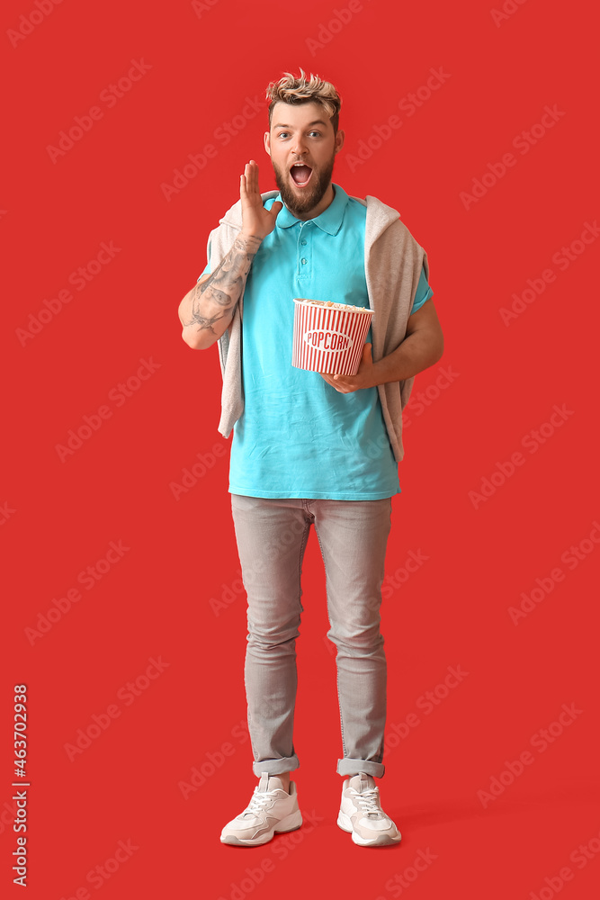 Surprised young man with popcorn on color background