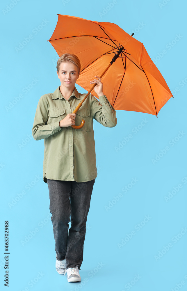 Young woman with open orange umbrella on blue background