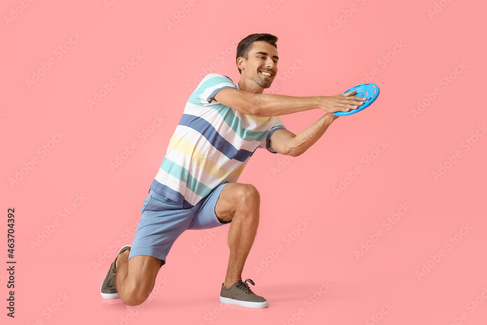 Handsome young man catching frisbee on pink background