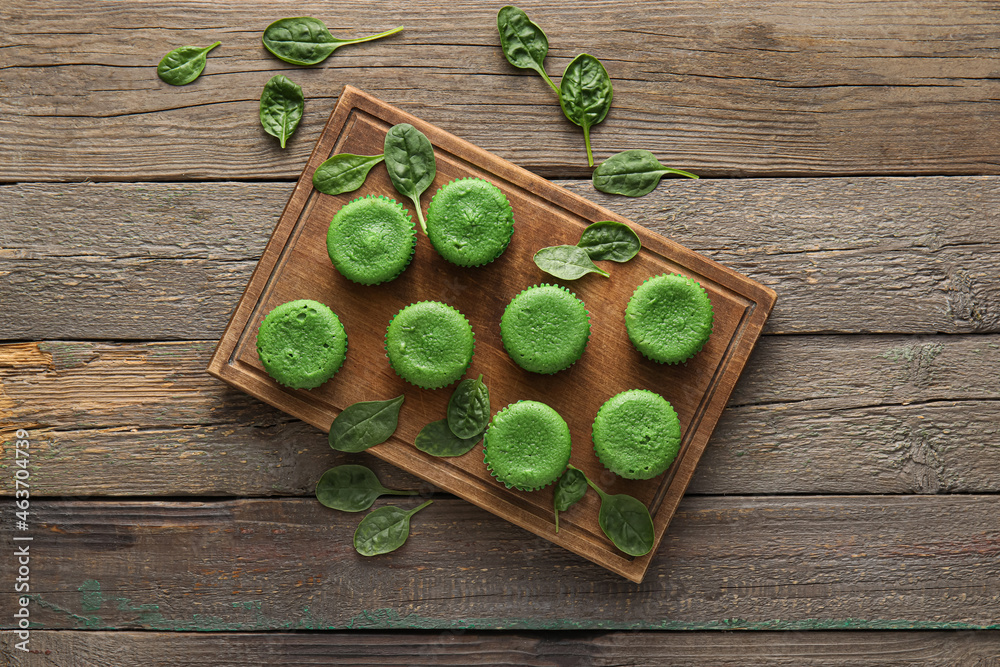 Board with tasty spinach muffins on wooden background