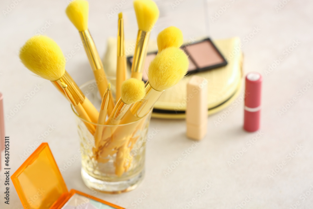 Glass with stylish makeup brushes on light table, closeup