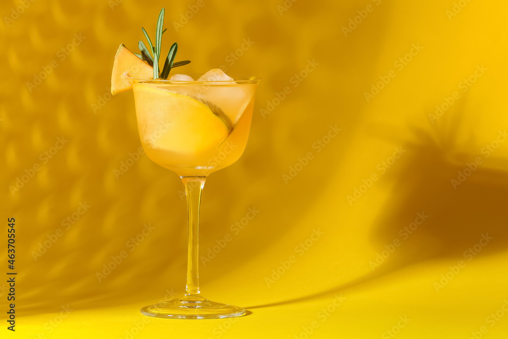 Glass of tasty melon cocktail on yellow background