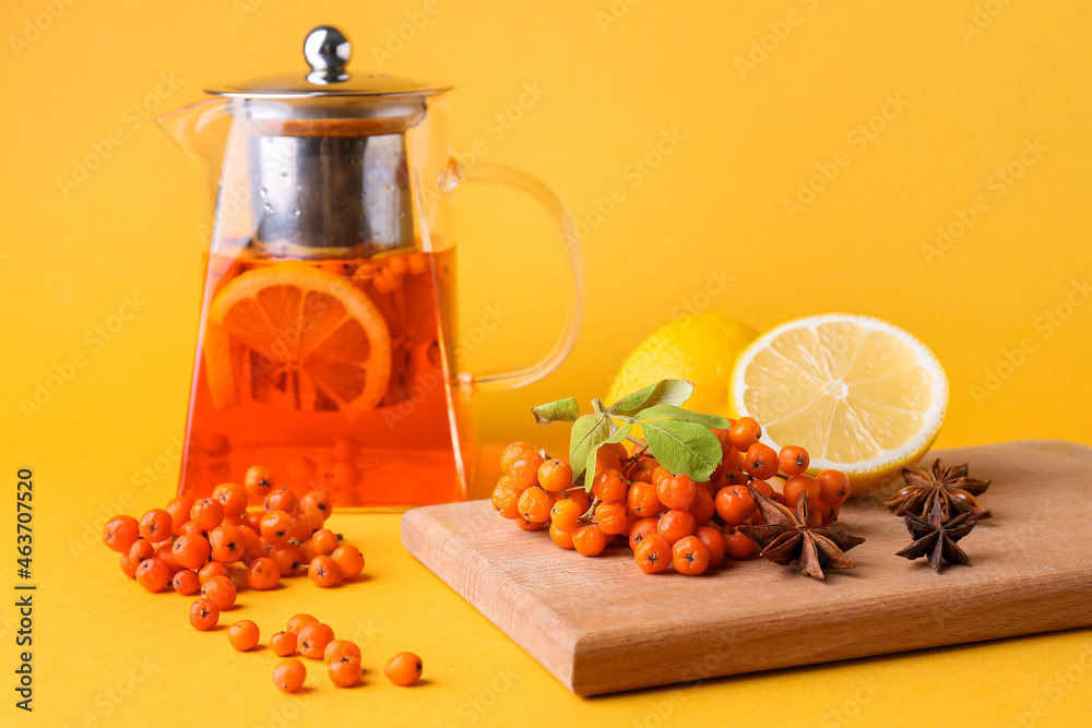 Composition with teapot of tasty rowan tea, lemons and berries on color background