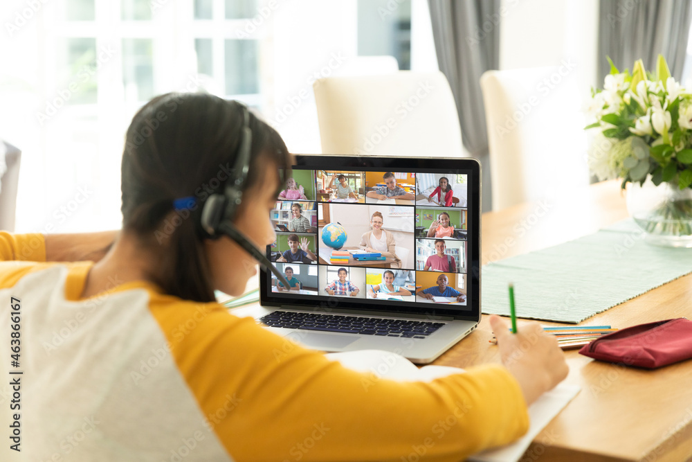 Asian girl using laptop for video call, with smiling diverse elementary school pupils on screen