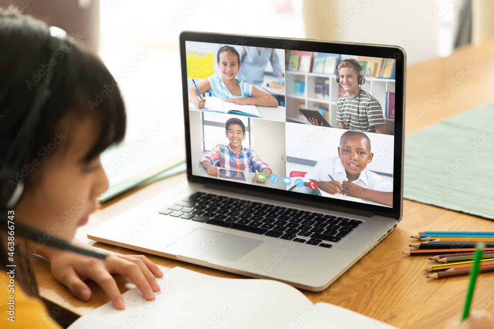 Asian girl using laptop for video call, with smiling diverse high school pupils on screen