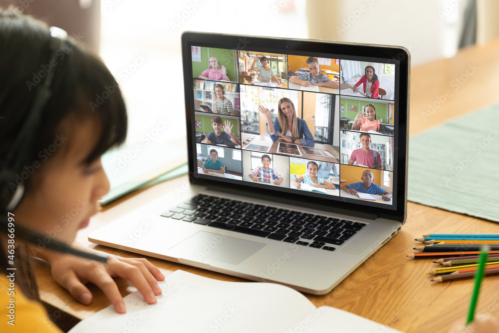 Asian girl using laptop for video call, with smiling diverse elementary school pupils on screen