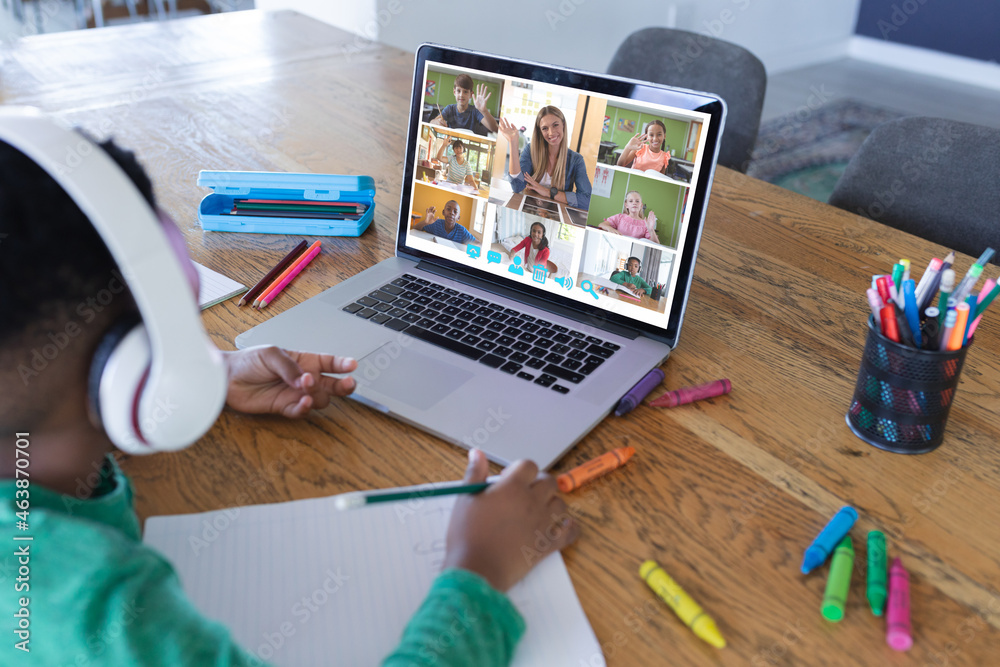 African american boy using laptop for video call, with diverse elementary school pupils on screen