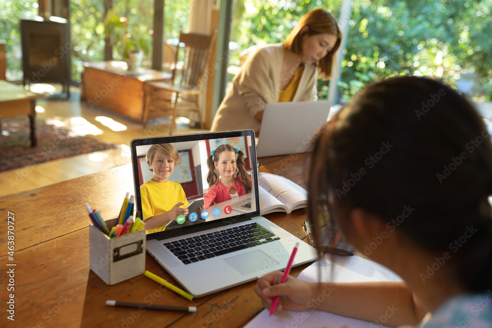 Asian girl using laptop for video call, with smiling caucasian elementary school pupils on screen