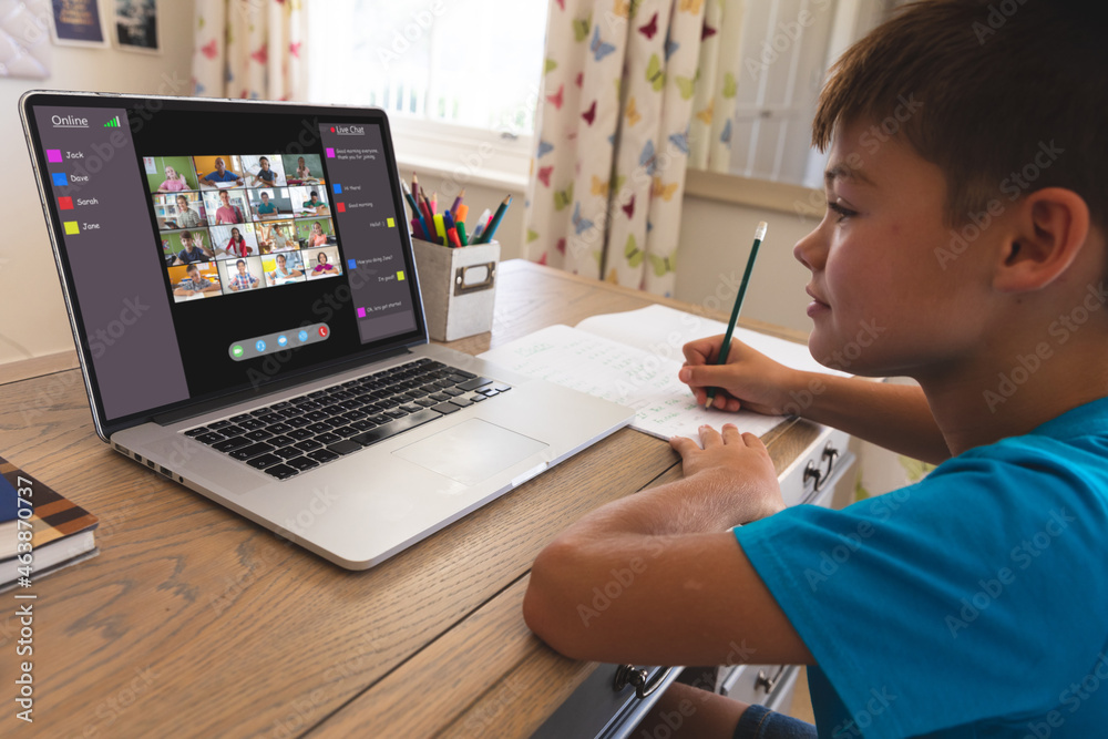 Smiling caucasian boy using laptop for video call, with diverse elementary school pupils on screen