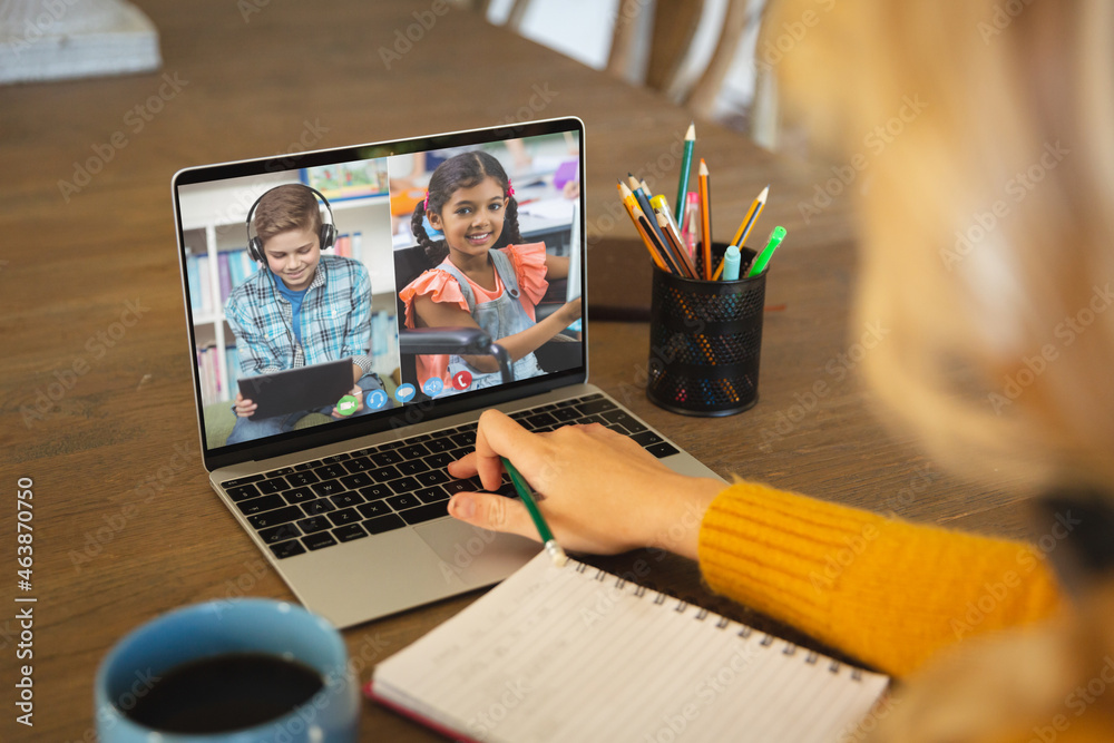 Caucasian woman using laptop for video call, with diverse elementary school pupils on screen