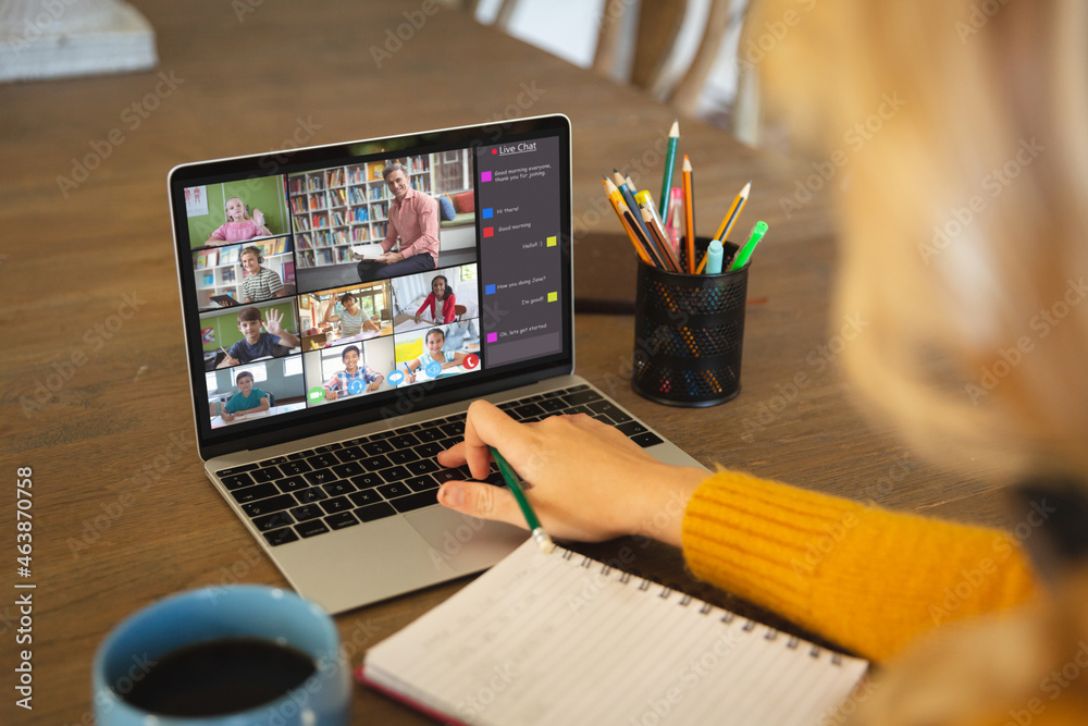 Caucasian woman using laptop for video call, with diverse elementary school pupils on screen