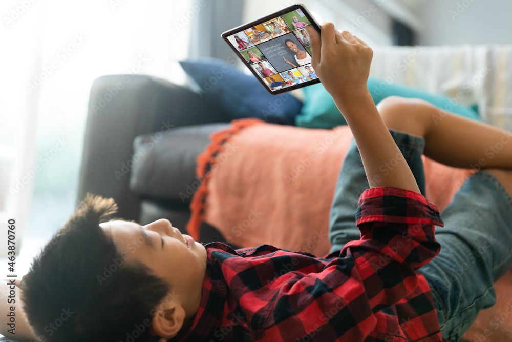 Smiling asian boy using laptop for video call, with diverse elementary school pupils on screen