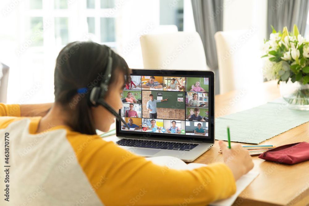 Asian girl using laptop for video call, with smiling diverse elementary school pupils on screen