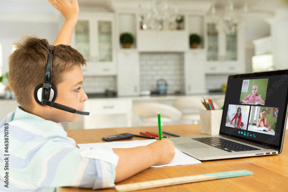 Caucasian boy raising hand for video call, with smiling diverse elementary school pupils on screen