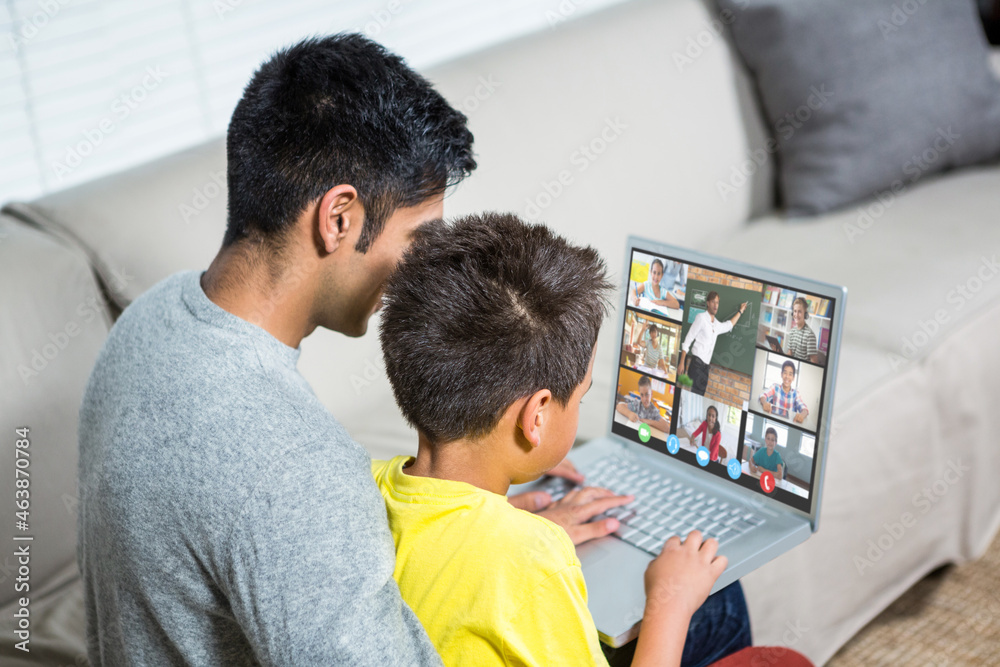 Biracial boy with father using laptop for video call, with elementary school pupils on screen