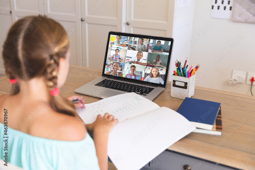 Caucasian girl using laptop for video call, with diverse elementary school pupils on screen