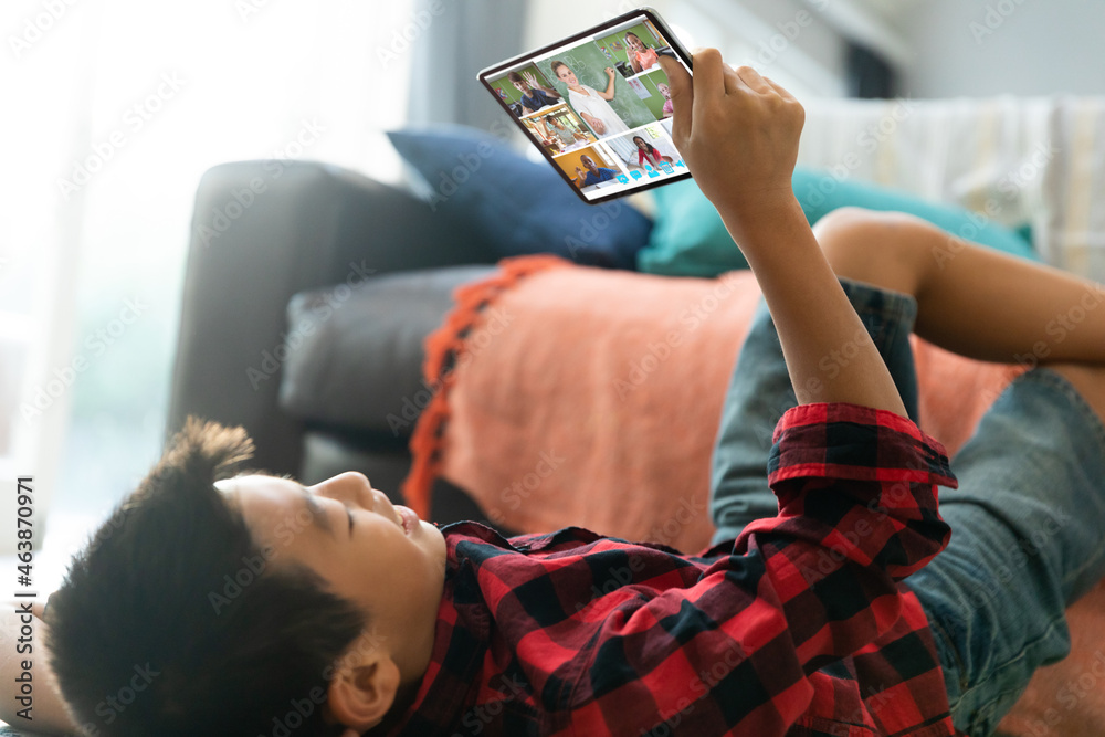 Smiling asian boy using tablet for video call, with diverse elementary school pupils on screen