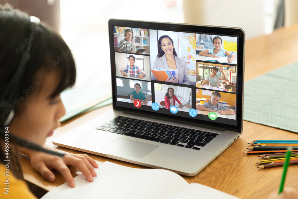 Asian girl using laptop for video call, with diverse elementary school pupils on screen