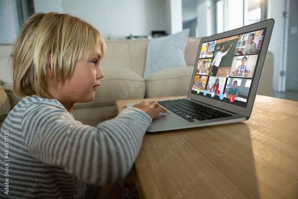 Smiling caucasian boy using laptop for video call, with diverse elementary school pupils on screen