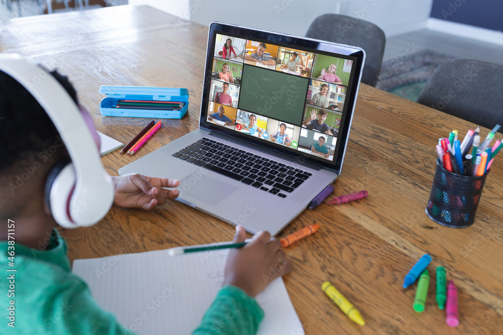 African american boy using laptop for video call, with diverse elementary school pupils on screen