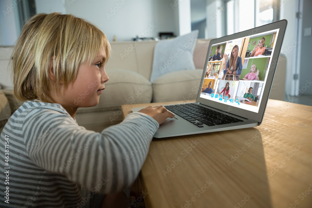 Smiling caucasian boy using laptop for video call, with diverse elementary school pupils on screen