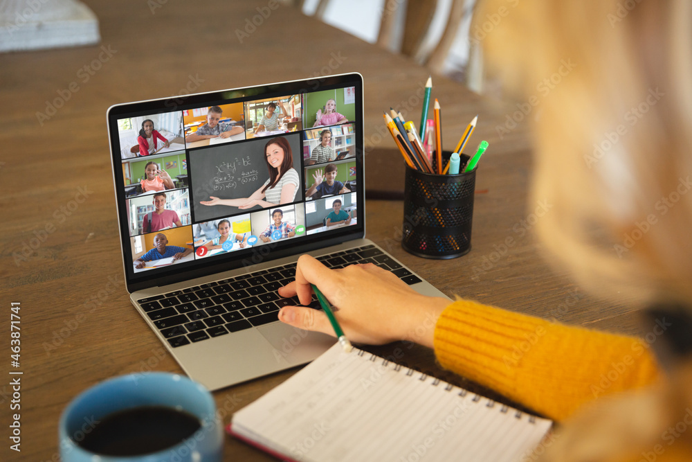 Caucasian woman using laptop for video call, with smiling diverse high school pupils on screen