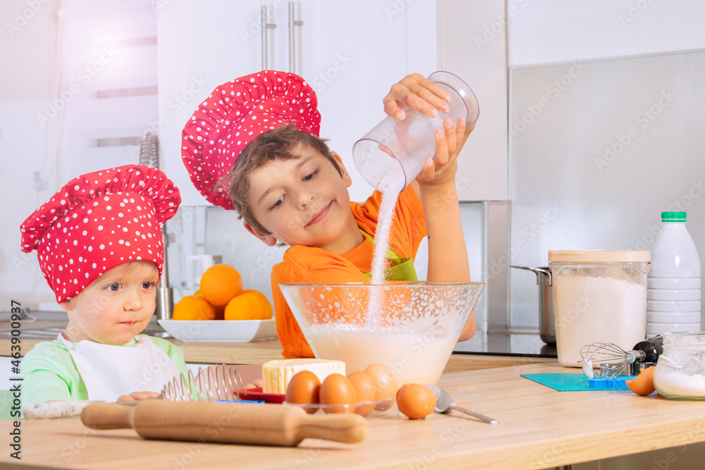 Boys cooking in chef hat add sugar to mixing bowl