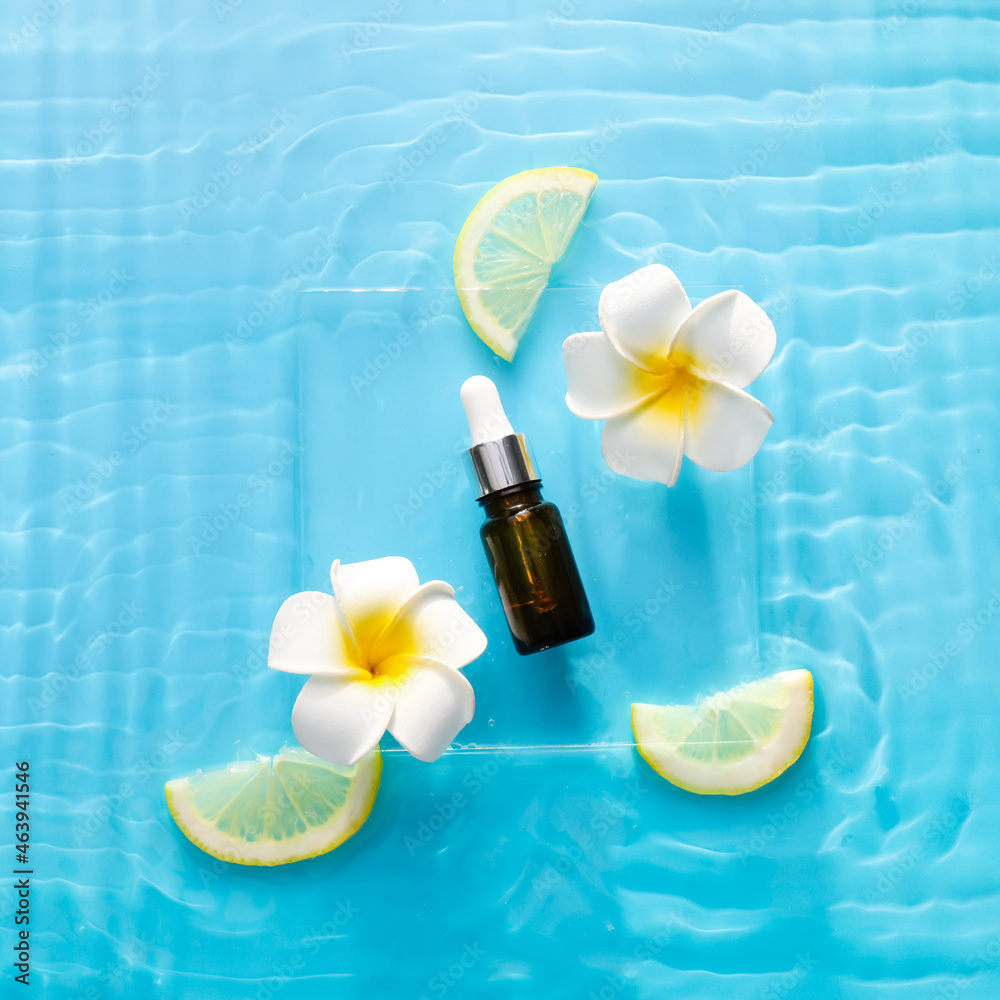 Cosmetic dropper bottle with flowers and lemon in water on color background