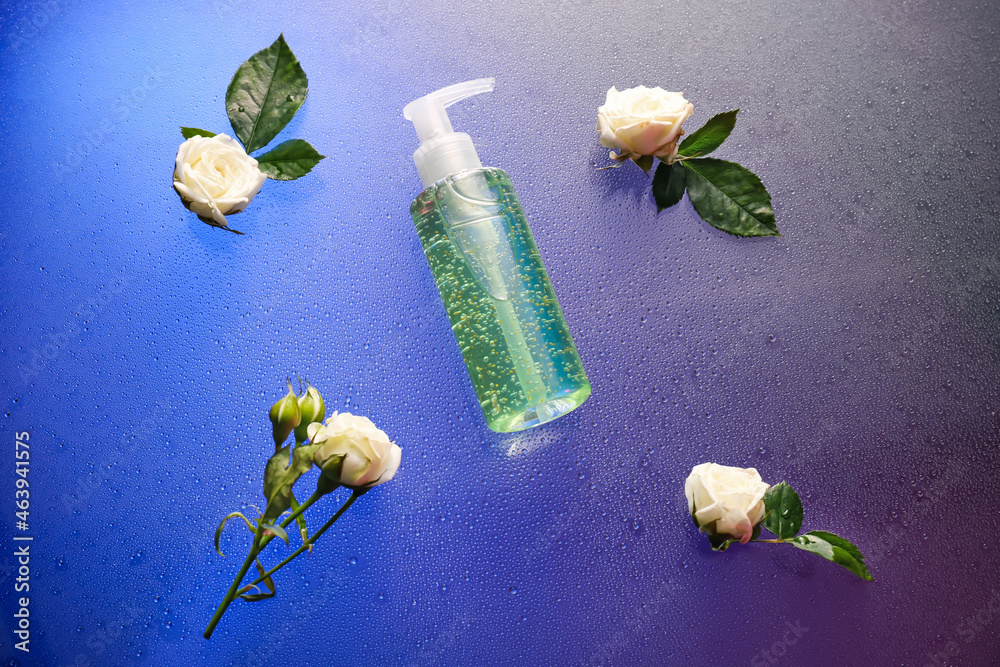 Bottle of cosmetic product and roses on color background with water drops