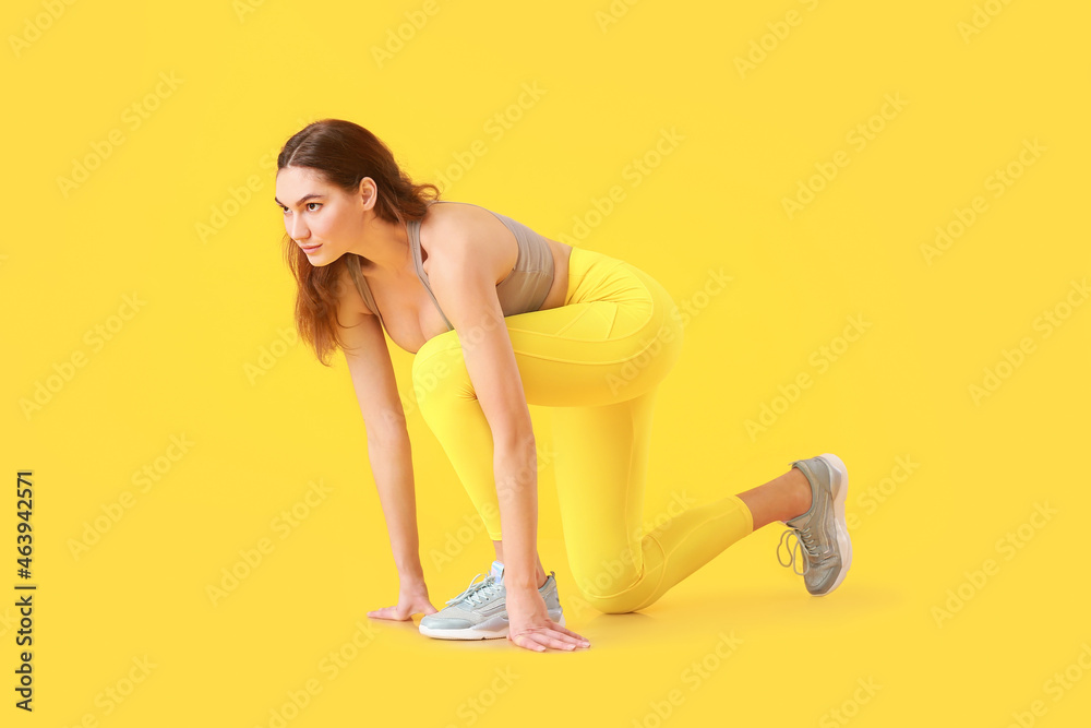 Sporty young woman in crouch start position on color background