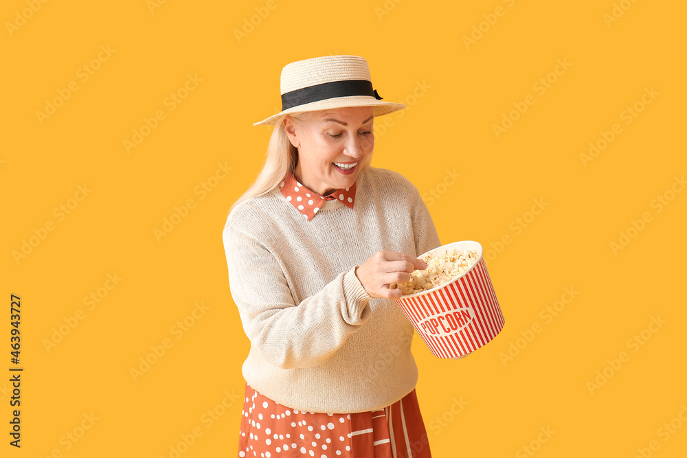 Mature woman with tasty popcorn on color background