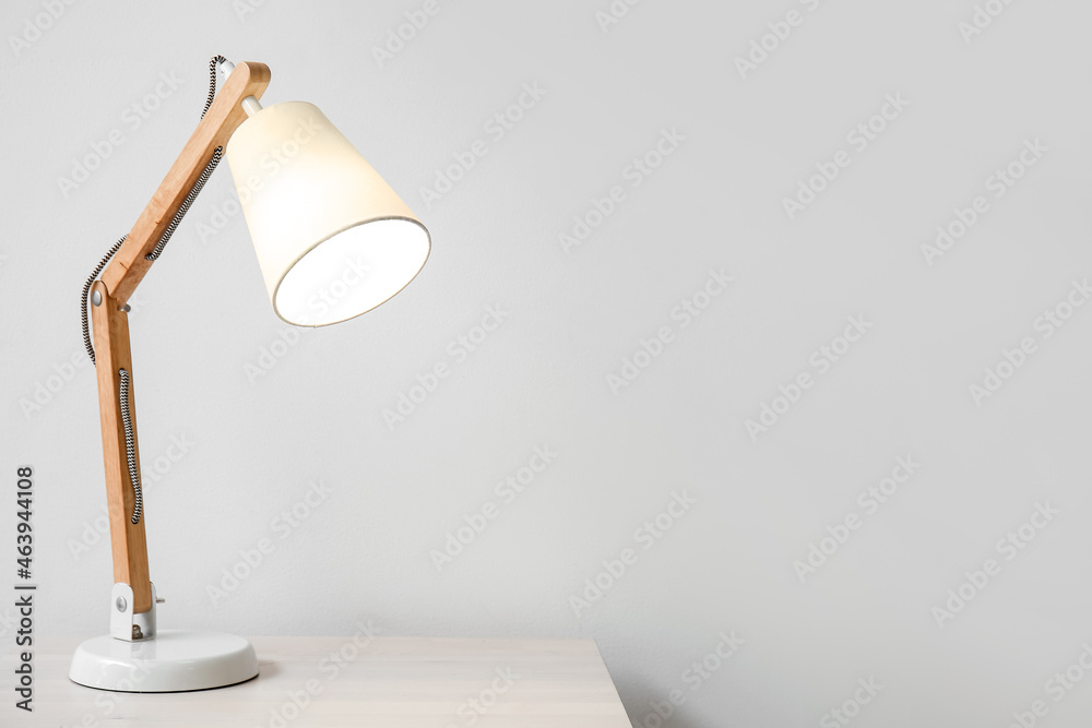 Wooden glowing lamp on table near white wall