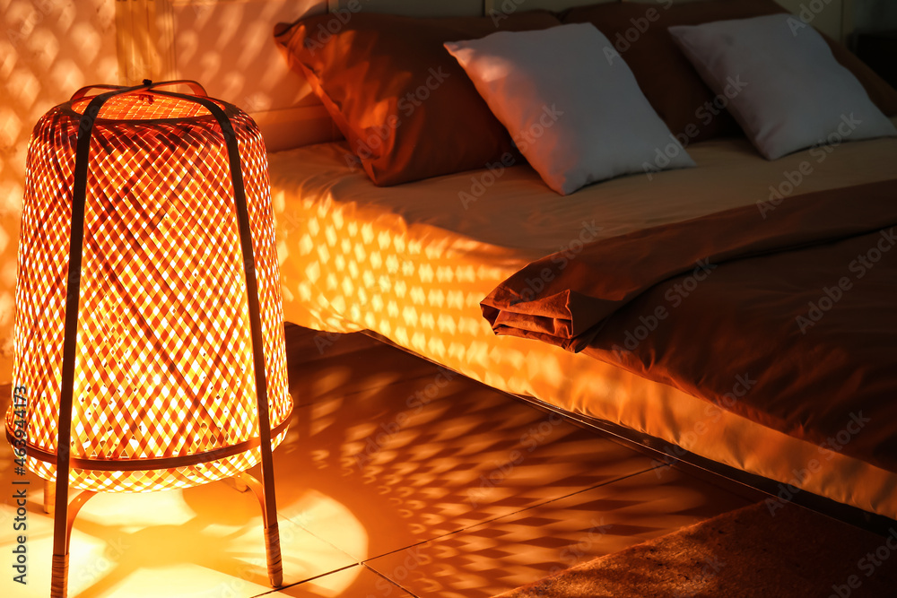 Glowing wicker lantern near bed in dark room