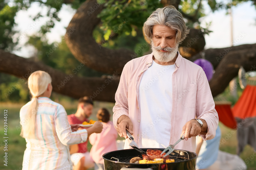 Senior man cooking food on barbecue grill outdoors