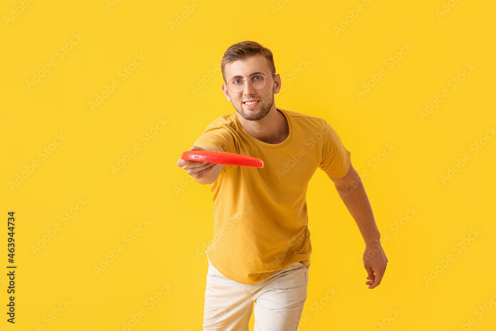 Handsome young man throwing frisbee on yellow background